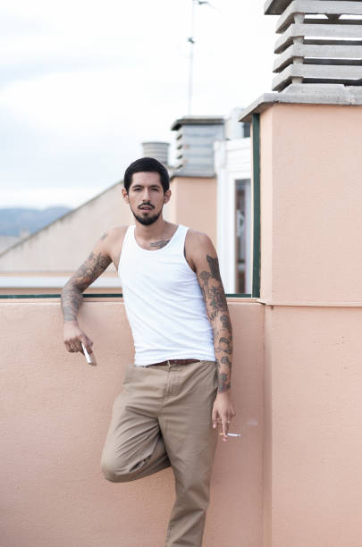 istock Young man with tattoos smoking a cigarette on a rooftop 2200029168