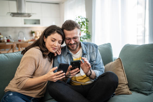 istock Cheerful young couple relaxing on sofa, browsing internet on smartphones 2200029267