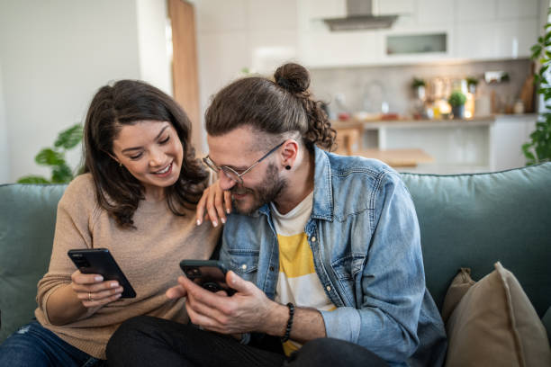 istock Cheerful young couple relaxing on sofa, browsing internet on smartphones 2200029275