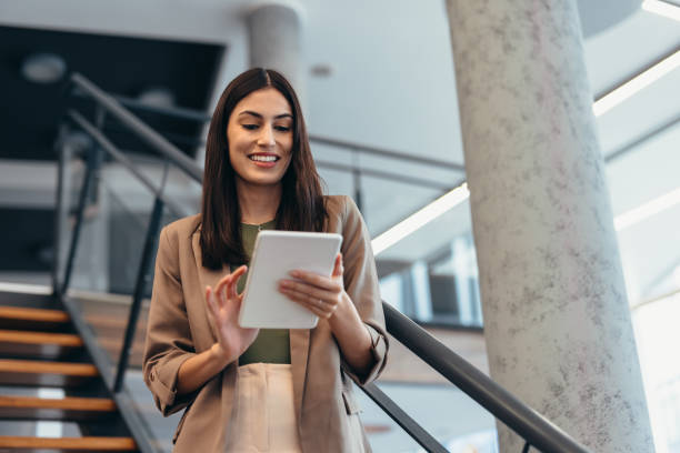 istock Smiling businesswoman using digital tablet while standing on stairs in modern office 2200031058