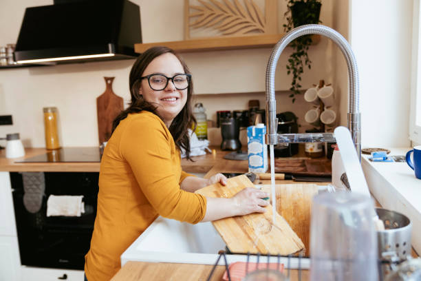 Young woman with Down Syndrome washing dishes in the kitchen stock photo