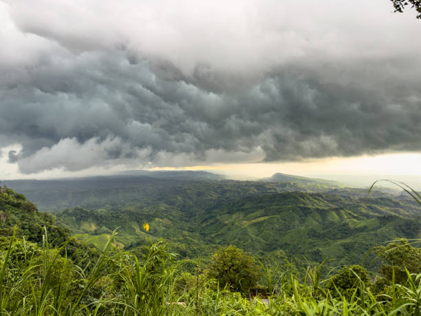 Dramatic storm clouds gather over the rolling green hills of Sajek Valley, Bangladesh, creating a stunning contrast between the dark sky and vibrant landscape, capturing the beauty of nature's power. extreme weather, storm clouds, Sajek Valley, Bangladesh landscape, mountain storm, monsoon season, tropical hills, cloudy sky, rural Bangladesh, dramatic sky, hilltop view, heavy rain clouds, weather change, green hills, nature storm, climate impact, overcast sky, storm brewing, valley scenery, scenic landscape