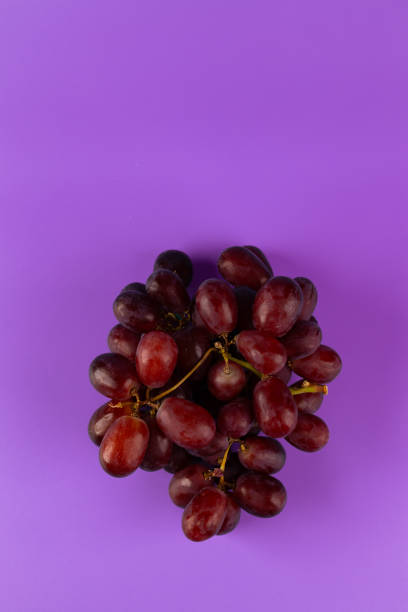 This image captures a cluster of fresh red grapes artfully arranged on a vivid purple backdrop, showcasing their natural color and texture, appealing to foodies and artists.
