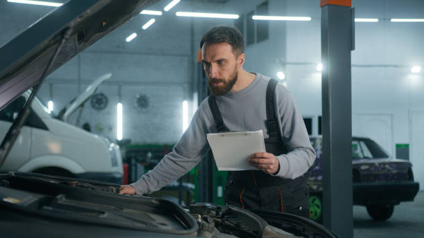 istock Caucasian auto mechanic specialist man checking engine with open bonnet write checklist in garage car service male technician check truck diagnostics vehicle automobile maintenance in repair workshop 2200047430