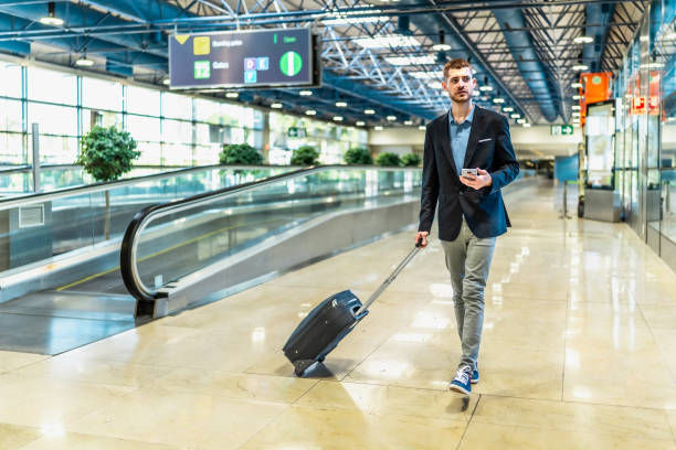 istock Businessman walking through airport terminal pulling suitcase and using smartphone 2200048661
