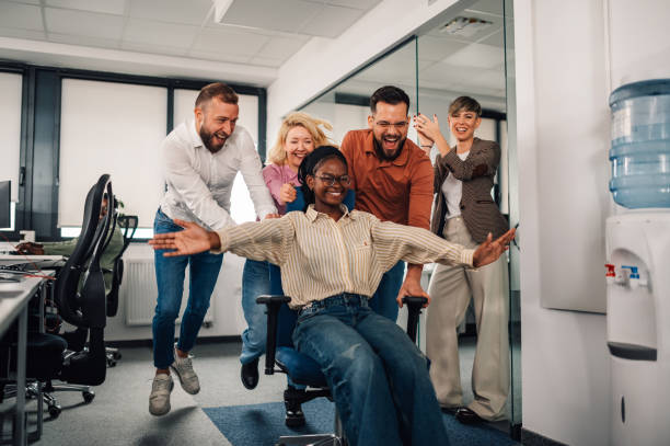 istock Business team pushing colleague on office chair, having fun at work 2200058594
