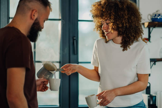 istock Woman pouring hot drink into mug for partner in kitchen 2200061777