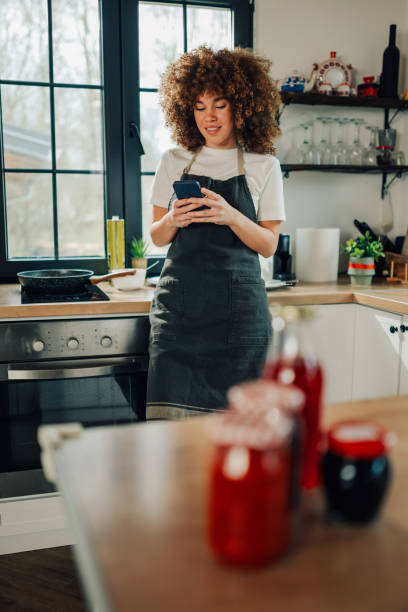 istock Smiling woman wearing apron using smartphone in kitchen 2200061799