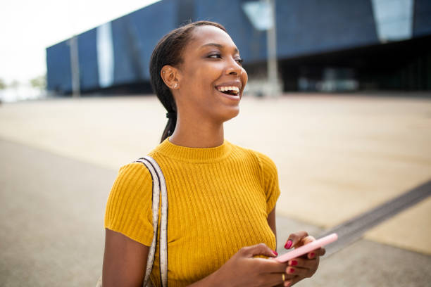 istock Cheerful black woman laughing while using mobile phone outdoors 2200065333