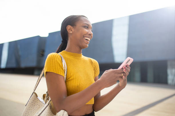istock Cheerful black woman laughing while using smart phone in city 2200065387