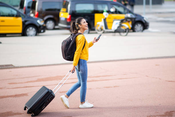 istock Full length happy young woman with mobile phone pulling suitcase in city 2200065631