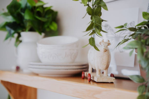 istock Decorative wooden cow figurine and white tableware on a shelf with plants 2200066116
