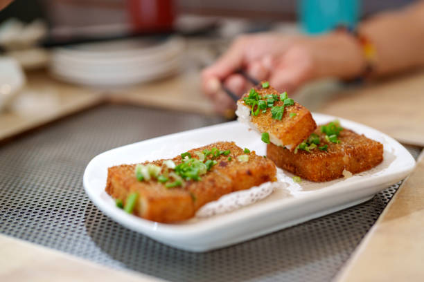 Close-up of crispy fried radish cake garnished with spring onions served on a white plate in a local restaurant.