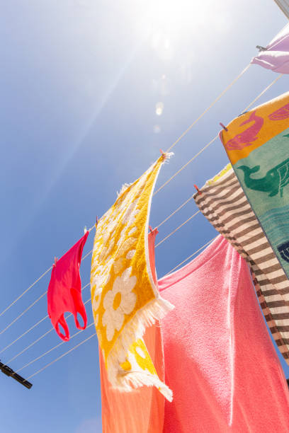 Freshly washed linens hanging on clothesline outdoors against blue sky with scattered clouds, fabric gently blowing in wind, natural drying process in open air environment