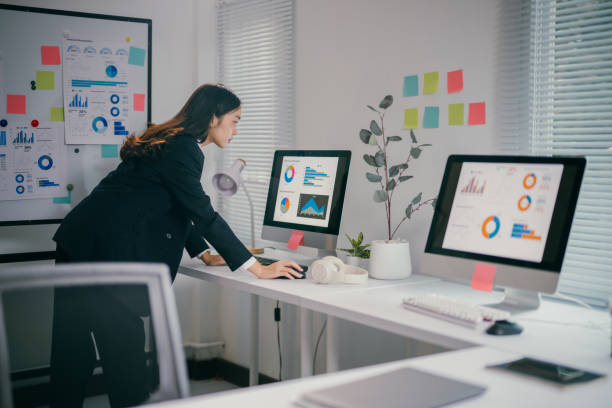 istock Professional woman analyzing financial data, bending over workspace with dual screens, embodying corporate workplace intensity in contemporary office environment 2200084704