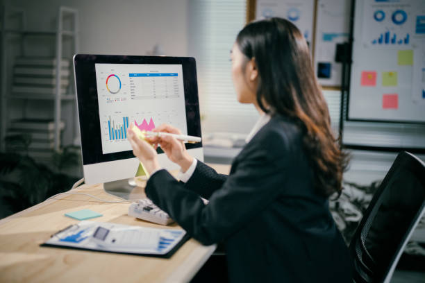 istock Professional businesswoman analyzing financial charts on computer screen, marking key data points with pen and sticky notes for strategic business planning 2200084734