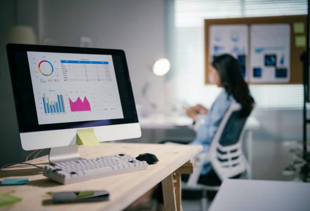 istock Corporate workspace featuring data analysis: laptop screen showing financial charts, wooden desk, professional woman working, emphasizing business performance tracking 2200085640