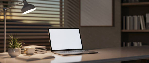 istock A laptop and decorative items sit on a table in a modern office, softly illuminated by a table lamp. 2200087915