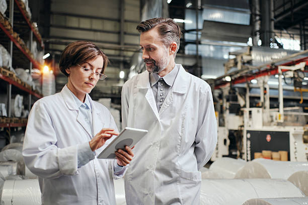 istock Two workers wearing uniform standing at factory warehouse with tablet 2200097647