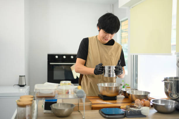 istock Smiling baker sifting flour for cookie dough in a bright kitchen 2200098103