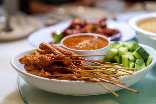 A plate of crispy Malaysian satay skewers served with rich peanut sauce and fresh cucumber slices, showcasing traditional street food flavors.