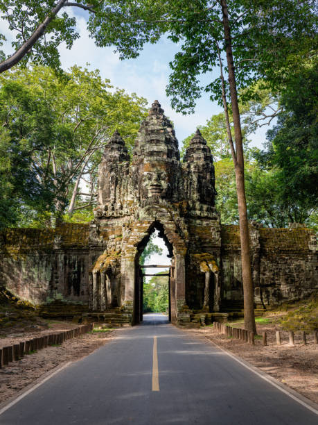 Angkor Thom North Gate Cambodia. Asphalt Road through the North Gate of Angkor Thom. Ancient Civilization Stone Entrance Gate with Religious Khmer Face Sculpture on Top of the North Entrance Gate towards the famous Angkor Thom Temple Area. Hasselblad X2D 102 MPixel High Detail Travel Shot with enough room to crop. Angkor Thom, Angkor Wat Area, Cambodia, South East Asia.