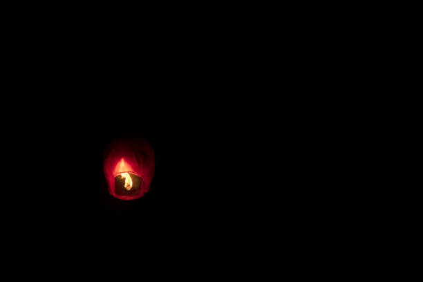 A vibrant sky lantern, also known as fanush, floating and glowing against a black night sky, creating a serene and festive atmosphere.