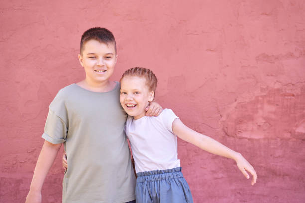 Happy siblings hugging in front of pink wall on a sunny day.