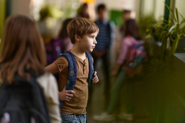 Elementary schoolboy feeling sad while standing out from the crowd in a hallway.
