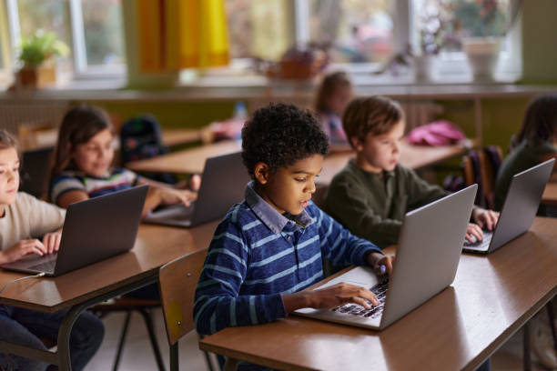 African American elementary student and his friends studying over computers during a class in the classroom.