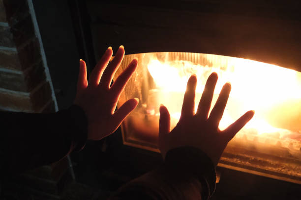 istock Two hands are held up close to a glass-enclosed fireplace, with flames visible inside, suggesting warmth and comfort. 2200114572