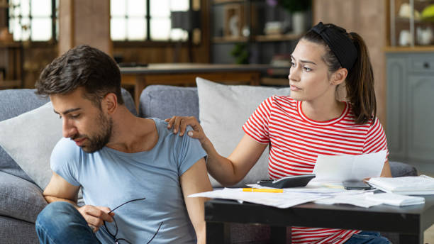 istock Couple calculating bills at home using tablet and calculator. Young couple working on computer while calculating finances sitting on couch. Young man with wife at home analyzing their finance with documents 2200116404