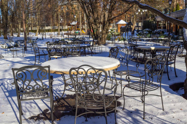 Empty winter cafe terrace. Round tables with snow and patterned metal chairs.