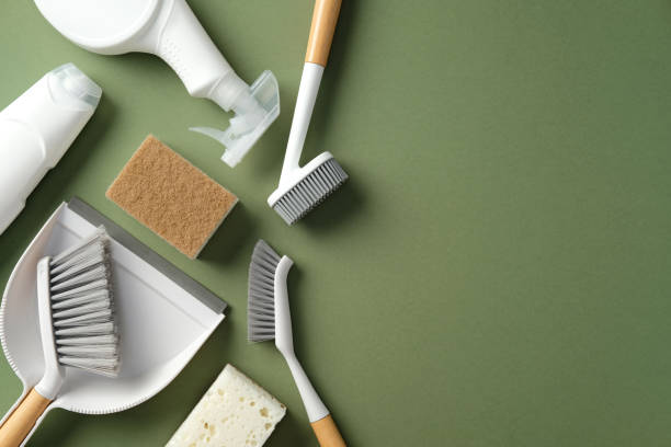 istock Cleaning supplies on a green background, including a spray bottle, sponge, scrub brushes, dustpan, and broom. Flat lay, top view. 2200116828
