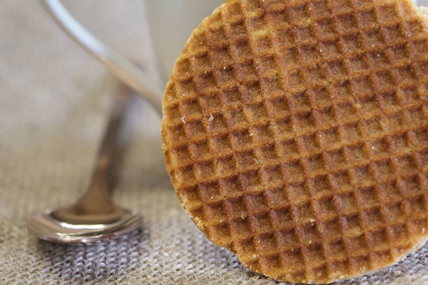 istock A close-up of a white mug with a caramel waffle cookie resting on its side, accompanied by a rose gold spoon, set on a textured burlap background. 2200118584