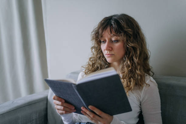 istock Young woman reading a book at home on the sofa 2200122746