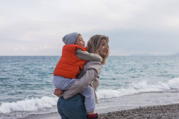 istock Mother carries son on her back while walking along the beach in winter 2200124120