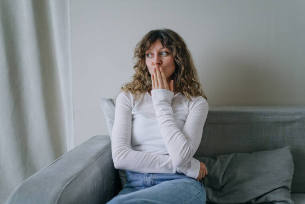 istock Shocked woman covering mouth while sitting on sofa at home 2200124568