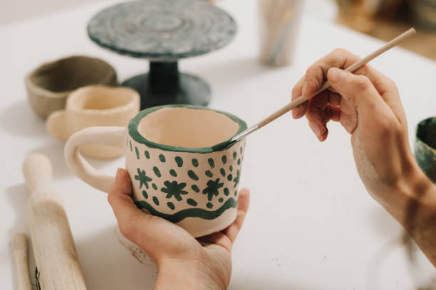 istock Design earthenware cup with a traditional pattern. Artist is making decoration on the clay ceramic mug after oven firing. 2200125594