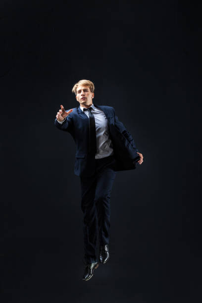 istock In a dark studio, a man in a sharp navy suit leaps mid-air, 2200125805