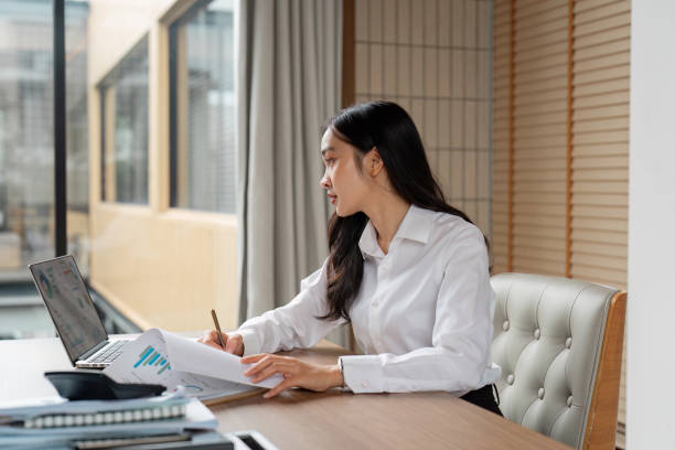 istock Focused young woman reviewing documents while working on a laptop. 2200125828