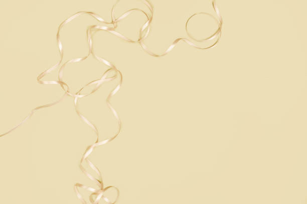 Light and shiny ribbons lay in a playful arrangement against a calm yellow background, perfect for adding elegance to events and crafts.