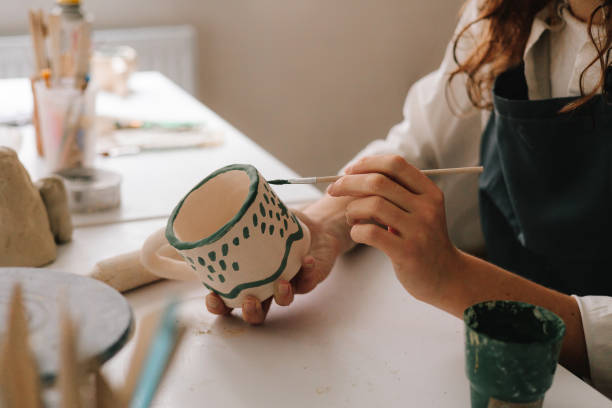 istock Experienced artist painting designs on ceramic cup in pottery workshop. Potter draws an abstract design into earthenware cup. 2200125961
