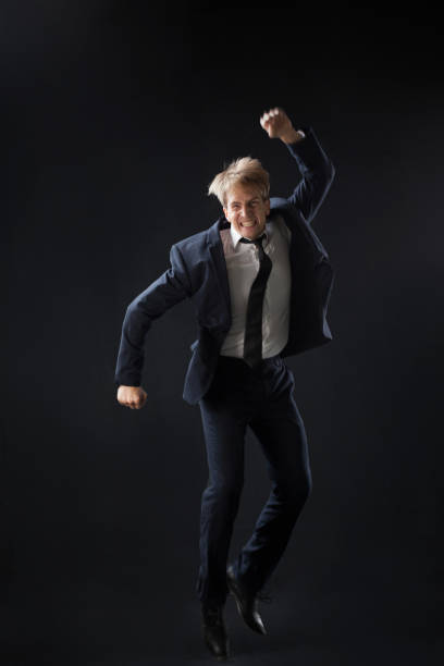 istock In a dark studio, a man in a sharp navy suit leaps mid-air, 2200126001
