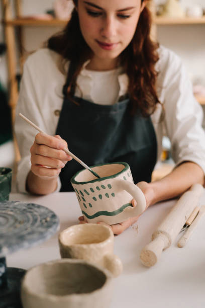 istock Experienced artist painting designs on ceramic cup in pottery workshop. Potter draws an abstract design into earthenware cup. 2200126064