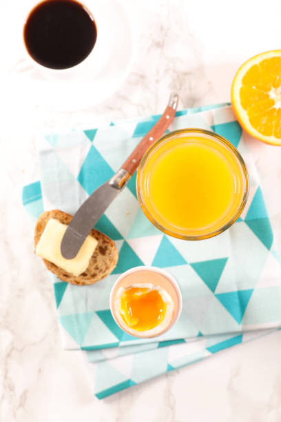 Stock photo showing close-up view of a white, china coffee cup and saucer, with a metal teaspoon, full of black, Americano coffee (espresso shot and water), a drinking glass of orange juice and plates with an all butter croissant and a plate of freshly baked biscotti (Italian almond biscuits), pictured against a mottled grey and white marble effect surface.