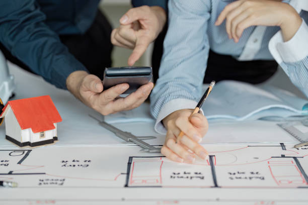 istock Engineers reviewing architectural plans and calculations with tools and a model house. 2200126593