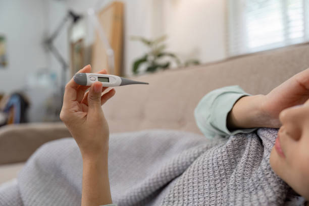 istock Concerned young woman checking her temperature with a digital thermometer while resting on a couch, highlighting health awareness. 2200126706