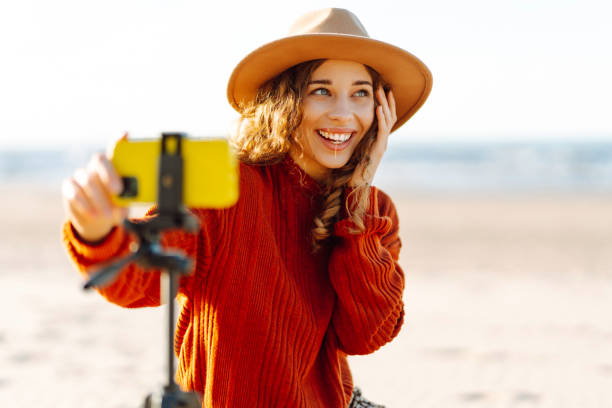 istock Young woman using smartphone with stabiliser  to create video content for social media on a sunny beach. 2200127443