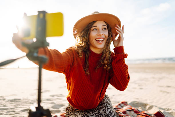 istock Young woman using smartphone with stabiliser  to create video content for social media on a sunny beach. 2200127452